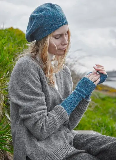 Blonde woman wearing blue beret and matching handwarmers against grassy background